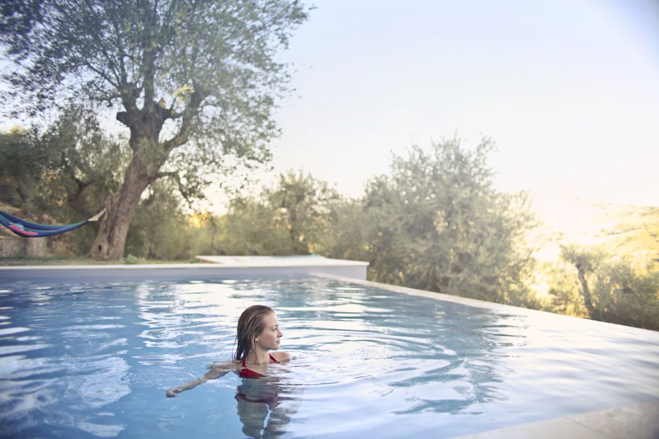 A woman in a red bikini enjoys a swim in a tranquil outdoor pool surrounded by lush greenery.